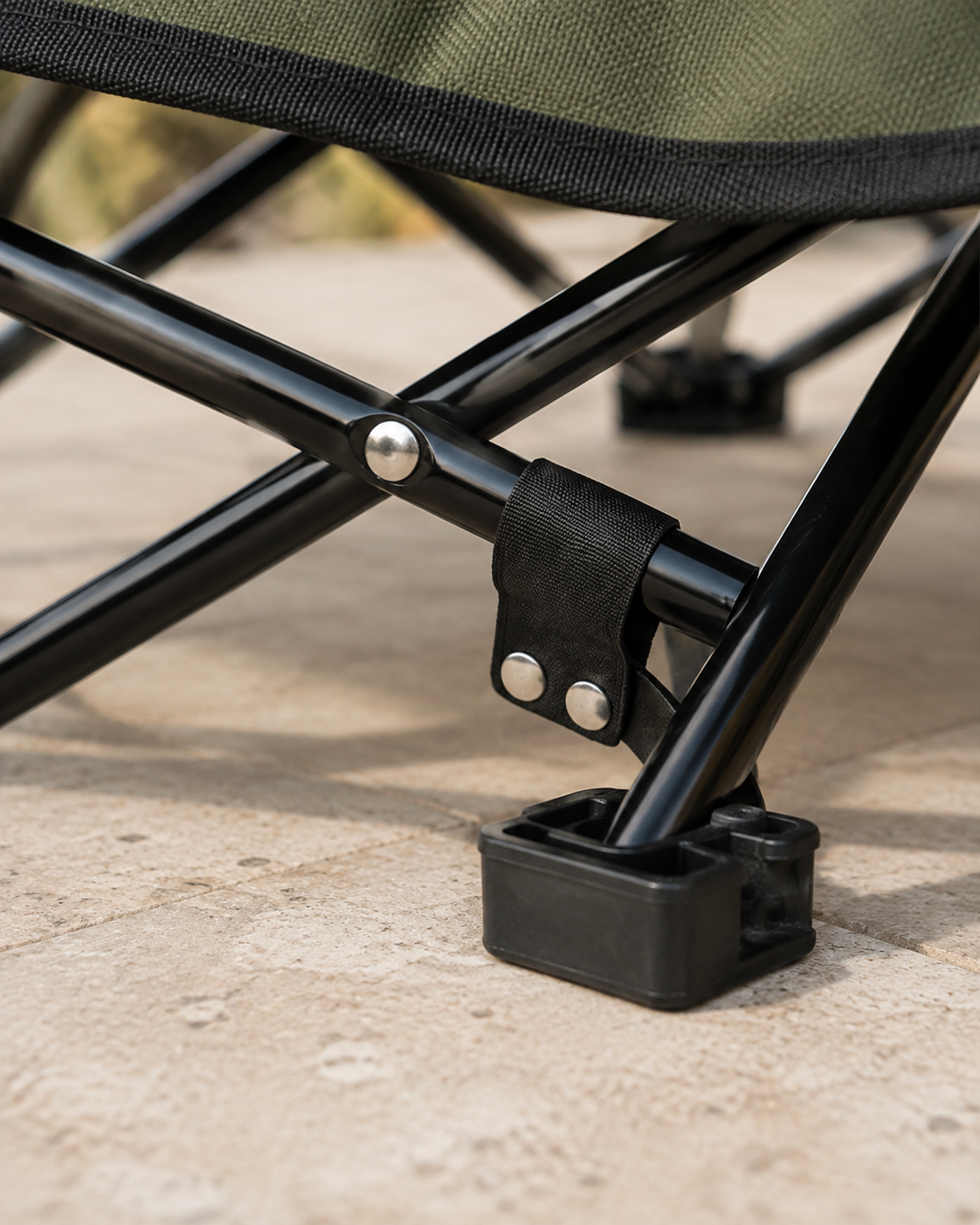 Green Camp Bed frame detail showing the crossing tubes, pivot, retaining strap and foot