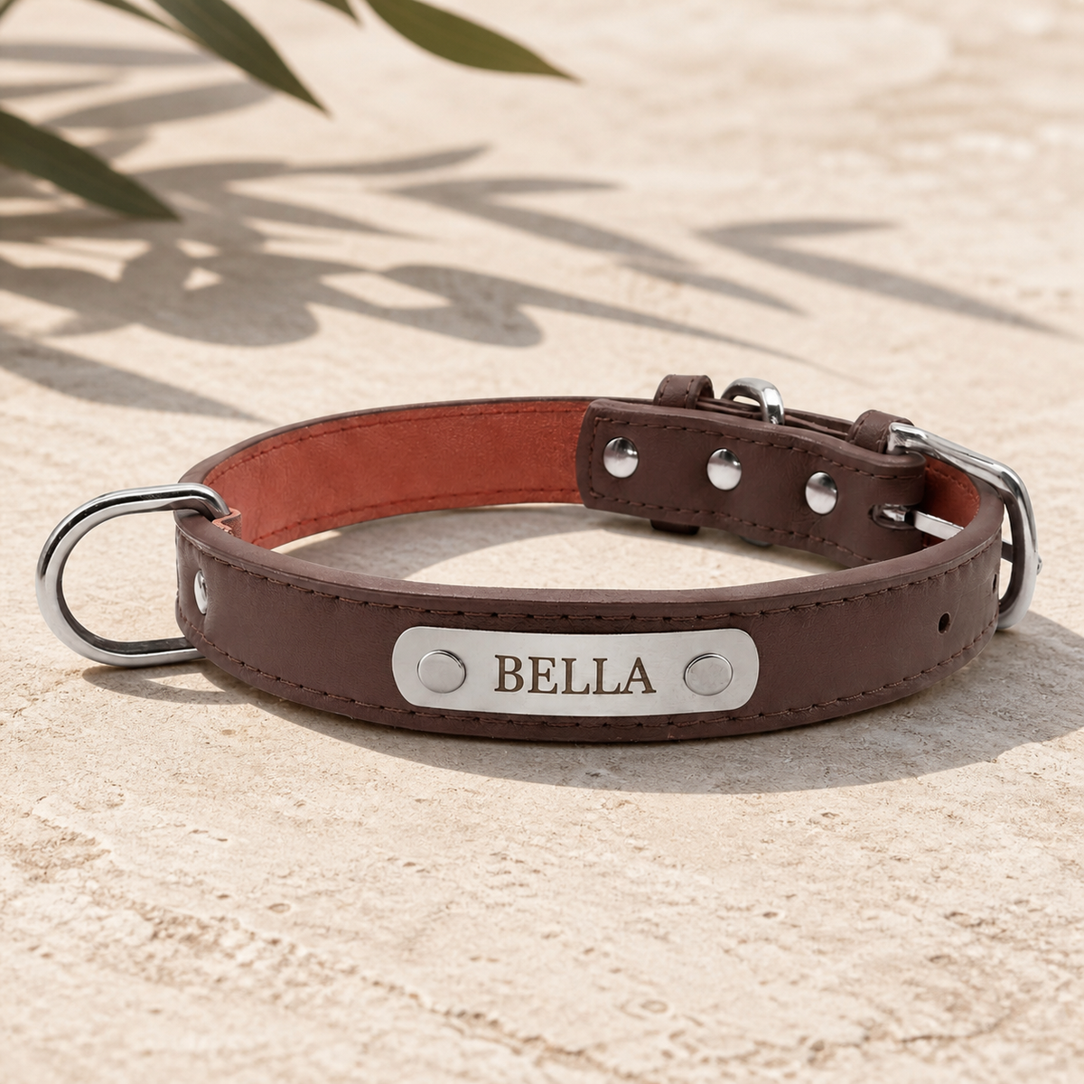 The Sutton Collar in brown leather with an engraved BELLA nameplate, resting on pale limestone